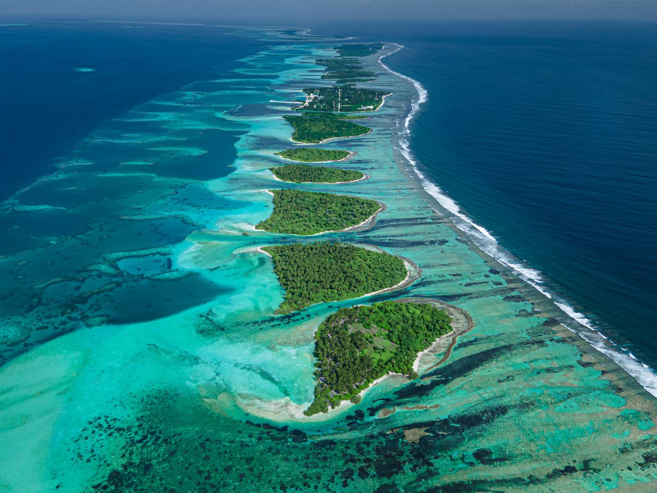 A breathtaking aerial shot of a Maldives atoll with vibrant blue waters and green islands.